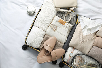 Open suitcase with folded clothes, shoes and accessories on bed, top view