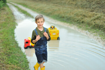 A little boy is playing with  toy cars in a huge puddle.
