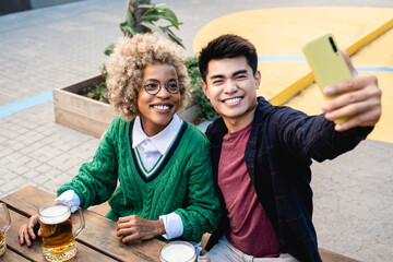 Happy multiracial friends doing selfie portrait having fun drinking beer at brewery bar - Focus on asian man