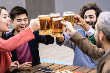 Multiracial friends having fun chearing with beers at brewery bar restaurant outdoor - Focus on