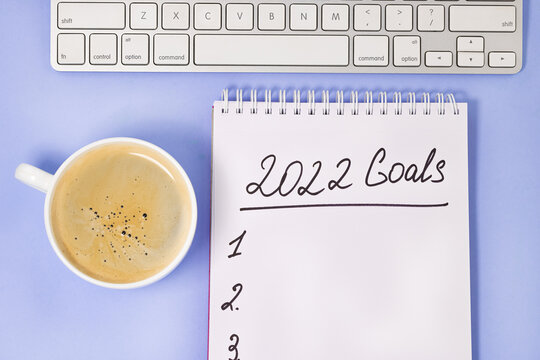 goals 2022 with keyboard and coffee cup on purple background. New Year resolutions and goal setting concept