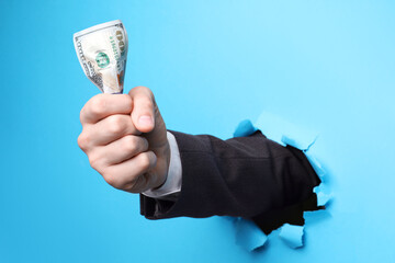 Businessman breaking through light blue paper with money in fist, closeup - obrazy, fototapety, plakaty