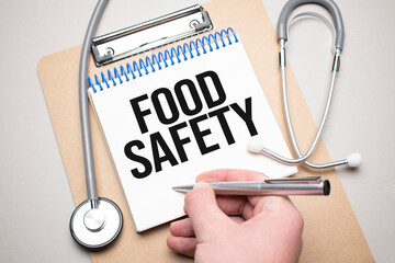 White notepad with the words food safety and a stethoscope on a blue background. Medical concept