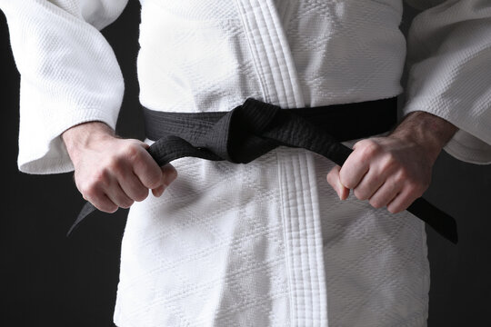 Karate coach wearing kimono and black belt on dark background, closeup