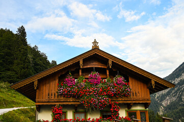 Front side of a traditional alpine house with beautiful flowers on the balcony and forested...