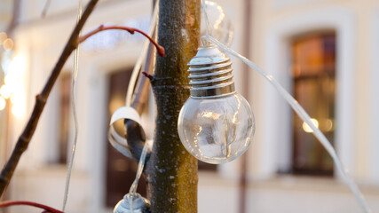 garland light bulb close-up. a garland wraps around the branches or trunk of a tree. incandescent light bulb close-up