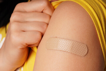 Bandage on young woman's arm after scratch on skin or injection for vaccine. A medical patch or plaster on a female shoulder after vaccination, selective focus
