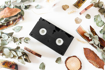 Video cassette, old-fashioned camera films, dried branches of eucalyptus leaves, and wood pieces on white background. Flat lay, overhead view, top view. Vintage frame composition.