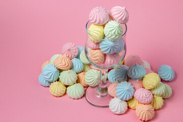 Multicolored meringues on a pink background. Glass goblet overflowing with colored meringues.