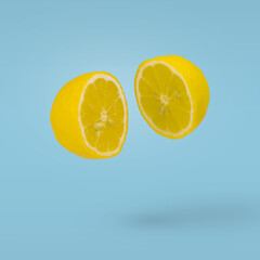 Juicy lemon cut in two halves flying in the air on a blue background. Summer citrus fruit refreshment.