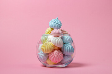 Multicolored meringues on a pink background. Glass vase overflowing with colored meringues.