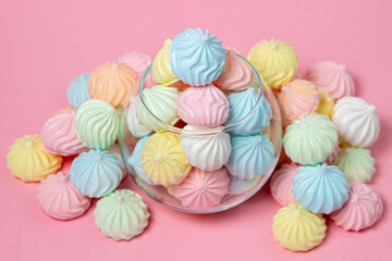 Multicolored meringues on a pink background. Glass vase overflowing with colored meringues.