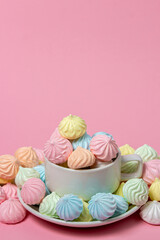Multicolored meringues on a pink background. A teacup overflowing with colored meringues.