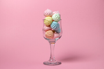 Multicolored meringues on a pink background. Glass goblet overflowing with colored meringues.