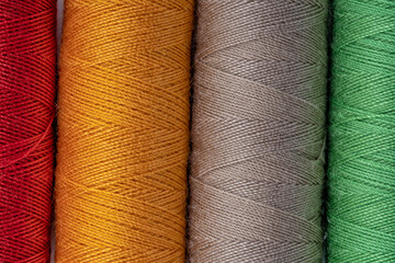 Four bobbins of sewing thread of red green orange and brown colors