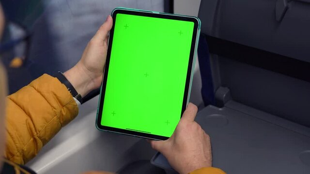 Back view of man watch tablet pc with green screen and browsing online in train. Mock up for watching content on pad. Blank digital phone in hand of guy sitting indoors in public transport