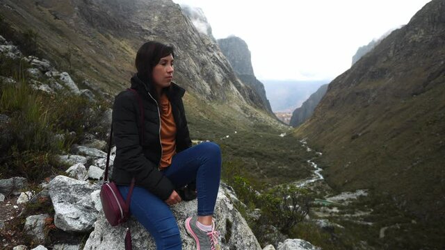 a beautiful woman sitting on a stone resting from climbing a hill next to a canyon in the Paron lagoon, Huaras