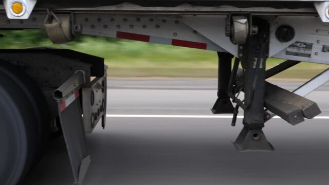 Driving beside tractor trailer. Detail of truck wheels, trailer and trailer hitch or fifth wheel.