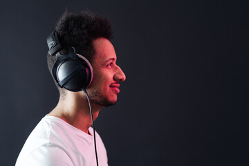 Smile Young African American man portrait wearing headphones and enjoy music over black Background. Red light reflection on face.