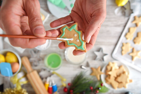 Detail of hands painting Christmas cookie and kitchen table background