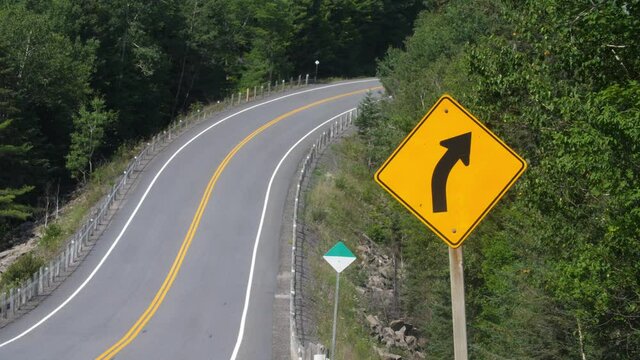 Highway corner with yellow and black arrow road sign. Summer driving on Highway 118 in Ontario, Canada. Medium shot.