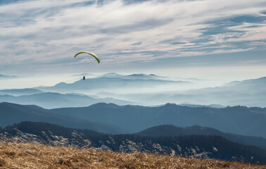 Paraglider flies in the sky over the mountains on a bright sunny day. Paragliding. Concepts:...
