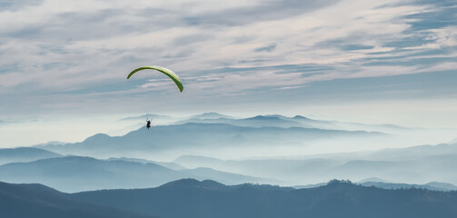 A paraglider soars in the sky over the foggy Carpathian valley. Paragliding. Concepts: adventure,...