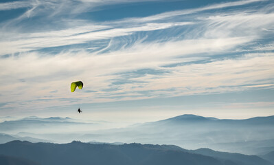 A paraglider soars in the sky over the foggy Carpathian valley. Paragliding. Concepts: adventure, determination, extreme sports. Alpine ski resort. Rest in Ukraine, Carpathian.