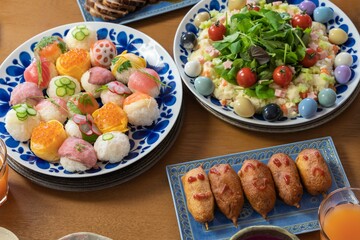 子供が喜ぶ楽しい食事が並んだパーティーの食卓（手毬寿司、カラフルなサラダ、チャーシュー、アメリカンドッグ）