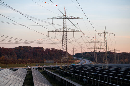 Renewable Energy, Large Field Of Solar Panels, Solar Panels And High Voltage Electricity Pylons Next To A Highway