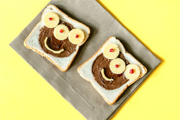 Funny monster face on halloween sandwich toast bread with peanut butter, cheese on napkin yellow background close up. Kids child sweet dessert breakfast lunch food
