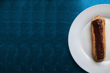 éclair au chocolat sur une assiette blanche et fond bleu 