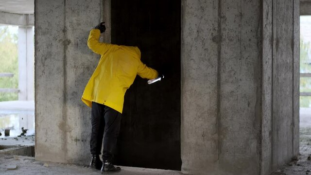 Inspection of old abandoned unfinished building by man in yellow overalls and flashlight. stalker in yellow raincoat and gas mask looks into abandoned elevator shaft.