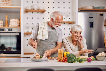 a happy senior couple preparing a healthy meal together, using a tablet