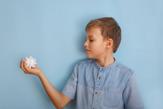 A boy in medicine mask against coronovirus on blue background. Kid is looking at the virus. Hand is holding model Coronavirus . Coronovirus molecule printed model on a 3D printer.