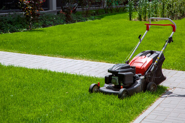 gasoline engine lawn mower for landscaping and backyard lawn mowing, gardening equipment on green grass surrounded by stone sidewalk walkway on a sunny summer day front view, nobody.