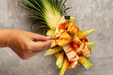 Cucumber, jicama and pineapple with chili powder and chamoy sauce on gray background. Mexican snack