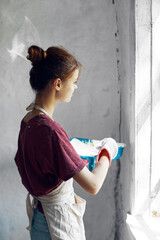 Woman in a white apron paints a window in a house interior renovation