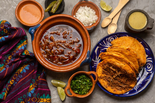 Birria tacos and broth on a gray background. Mexican food
