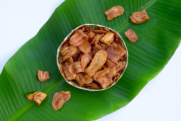 Banana slice chips in bamboo basket on banana leaf on white background.