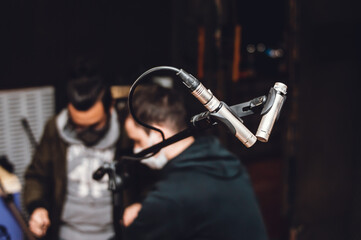 two condenser microphones mounted on a tripod, with two people blurred in the background.