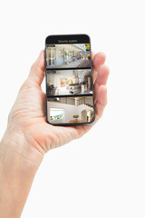 Hand of caucasian man holding smartphone with view of home from security cameras on screen