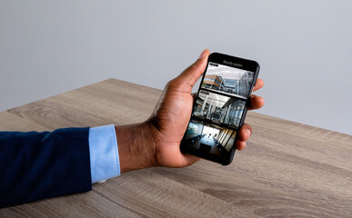 Hand of african american man holding smartphone, views of offices from security cameras on screen