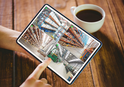 Hands of caucasian woman using tablet with view of warehouse from security cameras on screen