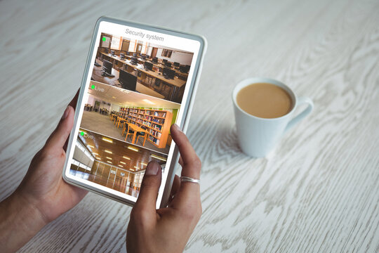 Hands of african american woman using tablet with view of library from security cameras on screen
