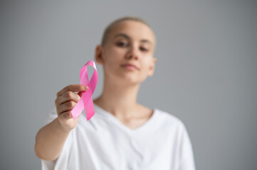 A faceless woman wearing a white t-shirt holds a pink ribbon as a symbol of breast cancer on a white background.