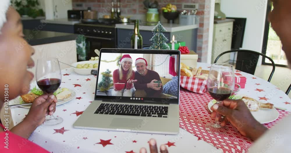 Canvas Prints African american couple with wine using laptop for christmas video call with happy couple on screen