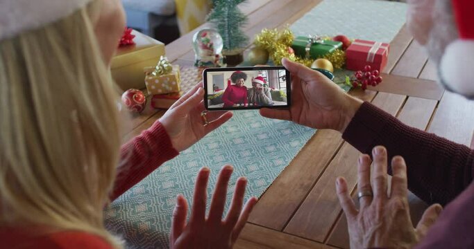 Caucasian couple with santa hats using smartphone for christmas video call with family on screen