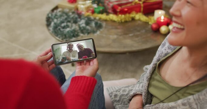 Smiling asian couple using smartphone for christmas video call with happy family on screen