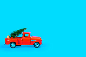 a red vintage car carries a green Christmas tree on a blue background in the back.